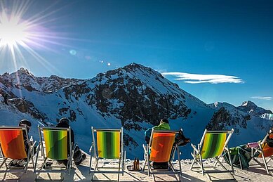 Einige Liegestühle auf dem Gipfel eines Berges mit Blick in die Berge bei Sonnenschein