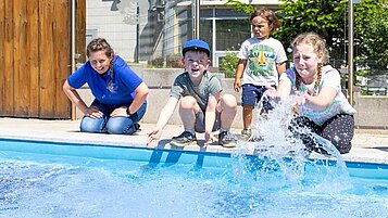 Kinder planschen gemeinsam mit einer Kundenbetreuerin im Wasser des Outdoor Pools im Family Club Harz 