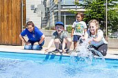 Kinder planschen gemeinsam mit einer Kundenbetreuerin im Wasser des Outdoor Pools im Family Club Harz 