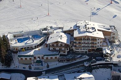 Winter-Luftaufnahme vom Wellness- & Familienhotel Egger in Saalbach Hinterglemm mit Skipiste.