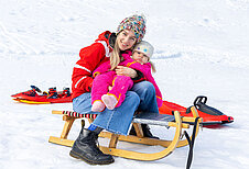 Mutter fährt mit ihrem Kind schlitten im Winter.