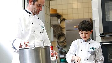 Gastgeber Alfred Boch begutachtet die Backkünste eines Jungen beim Kreieren einer Schwarzwälder-Kirschtorte.