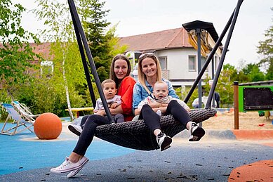 Mutter schaukelt ihr Kinder an auf dem Spielplatz vom Familienhotel Kolping Hotel Spa & Family Resort in Ungarn. 