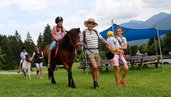 Ein Mädchen reitet auf einem Pony, begleitet von ihrer Familie auf einer Wiese des Familienhotels Ramsi in Kärnten