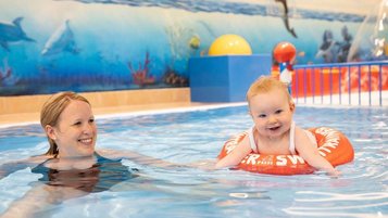 Mutter planscht mit ihrem Baby, das in einem Babyschwimmreifen sitzt, im Kinderpool des Familienhotels Kaiserhof in Tirol.