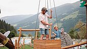 Vater und Sohn spielen auf dem Außenspielplatz vom Familotel Habachklause mit dem Seilzug