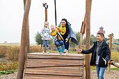 Mutter und Vater spielen gemeinsam mit ihren beiden Kindern auf einem Outdoor Spielplatz des Familienhotels Seeklause an der Ostsee.