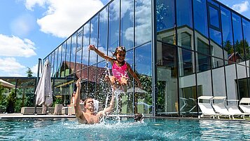 Familie planscht im großen Outdoor-Pool des Familienhotels Ulrichshof im Bayerischen Wald.