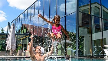 Familie planscht im großen Outdoor-Pool des Familienhotels Ulrichshof im Bayerischen Wald.