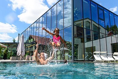 Familie planscht im großen Outdoor-Pool des Familienhotels Ulrichshof im Bayerischen Wald.