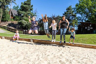 Kinder toben gemeinsam mit einer Kinderbetreuerin in der Sandkiste auf dem Außengelände vom Familienhotel Family Club Harz.