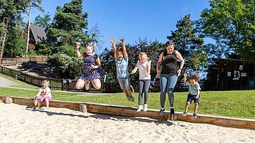 Kinder toben gemeinsam mit einer Kinderbetreuerin in der Sandkiste auf dem Außengelände vom Familienhotel Family Club Harz.