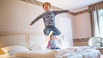 Kinder springen auf dem Bett im Familienzimmer des Familienhotels Borchard's Rookhus an der Mecklenburgischen Seenplatte.