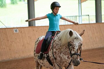 Kleines Kind nimmt Reitunterricht in der Reithalle des Schreinerhofs.