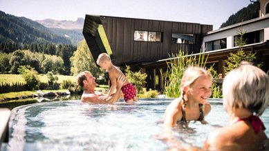 Familie mit zwei Kindern genießt gemeinsam den Außenpool des Alpura Retreats in den Bergen bei Sonnenschein und Naturkulisse.