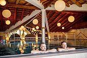 Ein Ehepaar entspannt am Beckenrand im Schwimmbecken des Familienhotels Das Hopfgarten in Tirol.