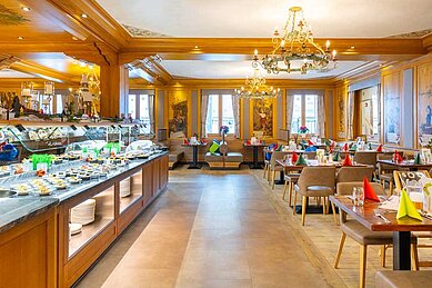 Elegantes Restaurant im Hotel Feldberger Hof mit einem reichhaltigen Buffet und dekorierten Tischen unter prachtvollen Kronleuchtern.