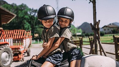 Zwei Mädchen sitzt auf dem Pferd und werden durch die Reitlehrerin geführt im Familienhotel Post Family Resort.