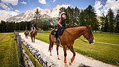 Kinder sitzen auf einem Pferd bei einem Reitausflug - im Hintergrund die Südtiroler Berge