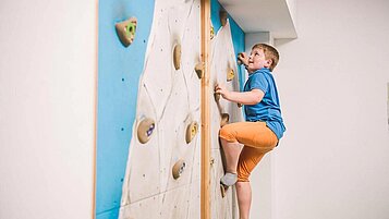 Junge klettert an der Indoor Kletterwand im Happy-Club des Familienhotels Landgut Furtherwirt in Tirol.