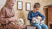 Kinder sitzen im Stall und streicheln Hasen im Familienhotel Almfamilyhotel Scherer in Tirol.