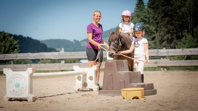 Kinder beim Ponyreiten mit Betreuung auf dem Reitplatz des Familienhotels Krone im Allgäu.