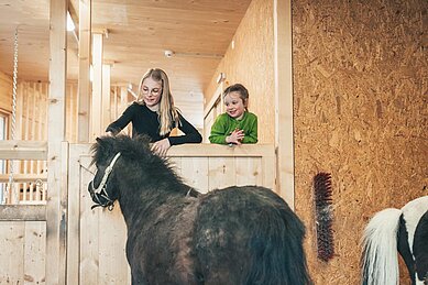 Zwei Kinder streicheln ein Pony im Stall im Familienhotel Almfamilyhotel Scherer in Tirol.