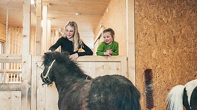 Zwei Kinder streicheln ein Pony im Stall im Familienhotel Almfamilyhotel Scherer in Tirol.