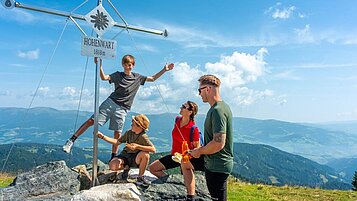 Familie am pausiert am Gipfelkreuz bei einer Wanderung im Familienurlaub in Kärnten