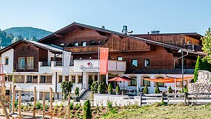 Das Familienhotel Das Hopfgarten in Tirol bei strahlenden Sonnenschein von außen. Auf dem Hotelgelände befindet sich ein großzügiger Outdoor-Spielplatz.