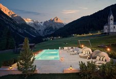 Der Außenpool im Familienhotel Bella Vista in Südtirol leuchtet am Abend mit Liegen, Sonnenschirmen und Bergkulisse.
