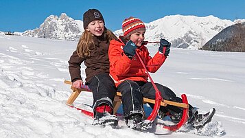 Kinder rodeln voller Freude die Piste hinunter in Südtirol im Familienhotel Alphotel Tyrol Wellness & Family Resort.