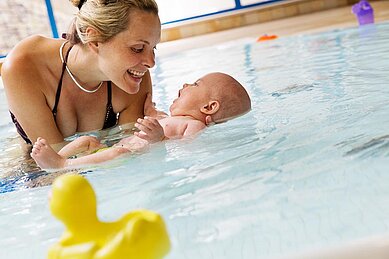 Mutter sitzt mit ihrem Baby im Babybecken und hält es im Arm im Wellness- & Familienhotel Egger in Saalbach Hinterglemm.