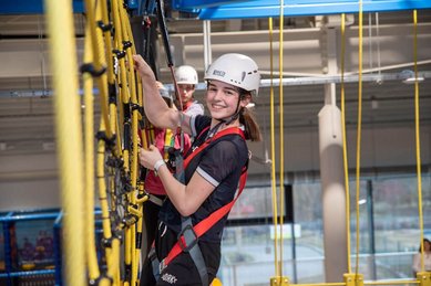 Hoch hinaus im Familienhotel Ungarn: Ein Mädchen meistert strahlend den Indoor-Kletterparcours im Kolping Family Resort und erlebt Action pur.