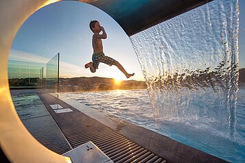 Kind springt draußen ins Schwimmbecken im Familienhotel Aigo welcome Family in Oberösterreich