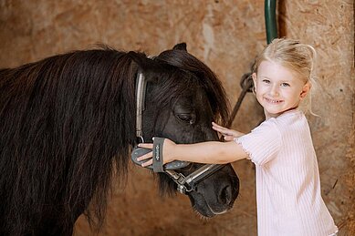 Mädchen streichelt ein Pony im Reitstall des Familienhotels Schreinerhof im Bayerischen Wald.