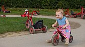 Das kleine Maedchen faehrt auf dem Spielplatz des Familienhotels Schreinerhof im Bayerischen Wald Dreirad.