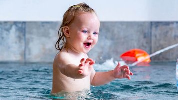 Glückliches Baby planscht im warmen Indoor-Pool des Familien Resort Petschnighof, einem Familienhotel in Kärnten mit Wasserspaß für die Kleinsten.