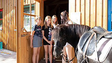 Mädchen stehen vor der Reithalle des Familienhotels Böhmerwald und streicheln ein Pferd.