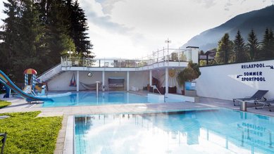 Außenpoolanlage im Familienhotel Egger mit Relaxpool, Sportpool und Kinderrutsche, umgeben von Bergen und Natur.