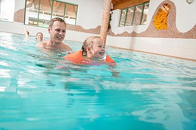 Eltern bringen ihrer Tochter im Schwimmbad des Familienhotels Landgut Furtherwirt das Schwimmen bei.