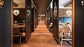 Gemütliches Restaurantinterieur mit Holzvertäfelung und -decken, stilvollen Pendelleuchten und traditionellen Stoffbänken, das eine warme und einladende Atmosphäre ausstrahlt.