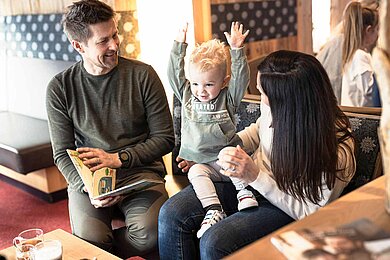 Familie sitzt mit Kleinkind im Hotel und schaut ein Buch an