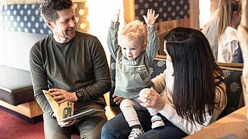 Familie sitzt mit Kleinkind im Hotel und schaut ein Buch an