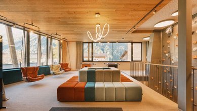 Moderner Aufenthaltsbereich für Teenager mit Kletterwand, Sitzgelegenheiten und Hängesesseln im Familienhotel Kindl