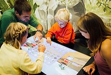 Eltern spielen mit ihren beiden Kindern ein digitales Brettspiel im Happy-Club des Familienhotels Sailer in Tirol.