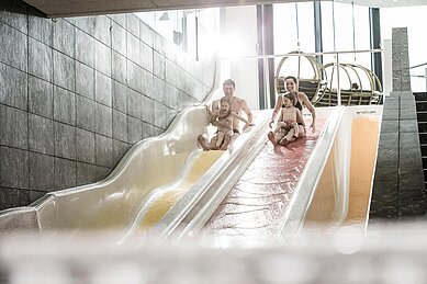 Eltern rutschen mit ihren beiden Kindern die Wasserrutschen im Familienhotel Allgäuer Berghof hinunter.