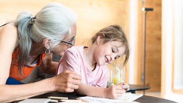 Eine Großmutter malt und lacht gemeinsam mit ihrer Enkelin in einem Familienhotel.