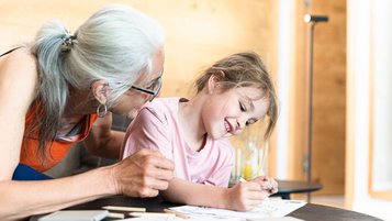 Eine Großmutter malt und lacht gemeinsam mit ihrer Enkelin in einem Familienhotel.