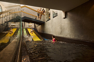 Familie mit zwei Kindern rutscht auf den Wasserrutschen im Schwimmbad des Familienhotels Alpenhotel Kindl ins Becken.